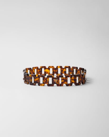 Prada reinterpreta la cadena clásica con una mirada moderna en este cinturón de plexiglás con efecto carey. Los eslabones rectangulares de líneas pulidas se articulan en una pieza ligera pero rotunda, rematada con el logo en letras doradas que sella su carácter contemporáneo. (1.200 €)