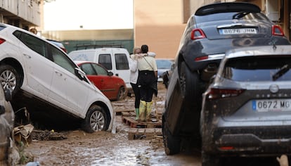 Dos personas se abrazan entre los coches amontonados en una calle de Paiporta, este viernes. 