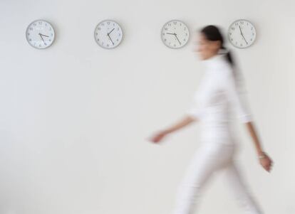 Una mujer pasa por delante de una pared con varios relojes.