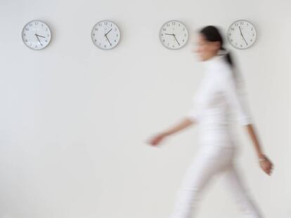 Una mujer pasa por delante de una pared con varios relojes. 