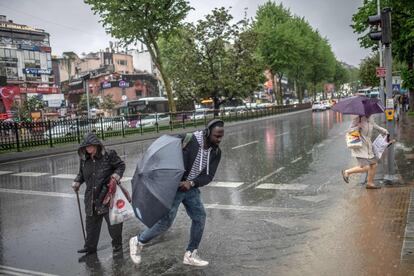 Varios peatones cruzan una calle encharcada tras las fuertes lluvias en el barrio de Besiktas, en Estambul (Turquía). 