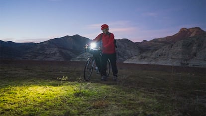 Un hombre con su bici en medio de la montaña anocheciendo.