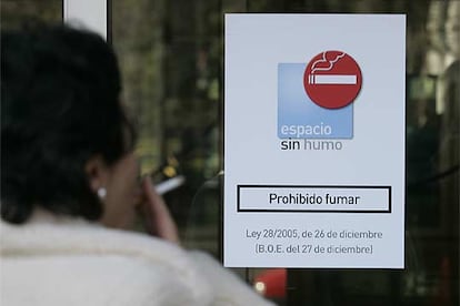 Una mujer fuma en la entrada del Ministerio de Industria, en Madrid, ante un cartel que prohíbe fumar en el interior.