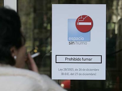 Una mujer fuma en la entrada del Ministerio de Industria, en Madrid, ante un cartel que prohíbe fumar en el interior.