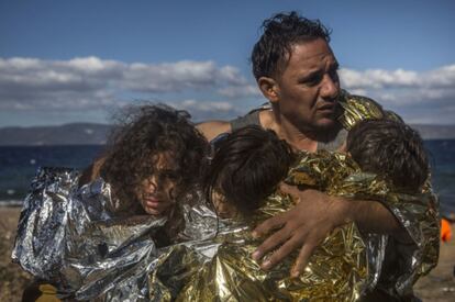 Un hombre sostiene a tres niños que se protegen con mantas térmicas a su llegada a la isla griega de Lesbos el 28 de octubre. SANTI PALACIOS (AFP)