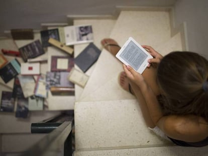 Una joven lee un libro electrónico junto a varios libros en papel.