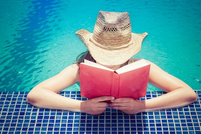 Woman wearing straw hat reading book at pool edge