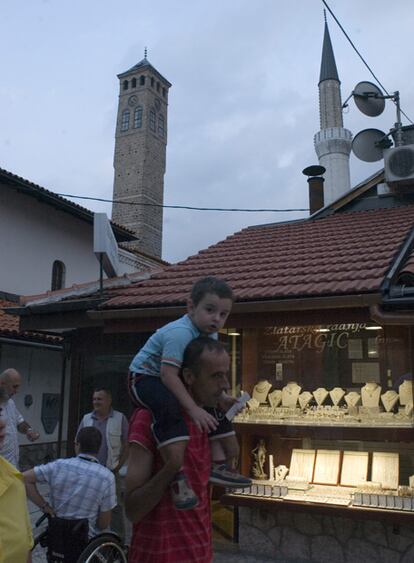 Un niño pasea a hombros de su padre en el centro de Sarajevo. Al fondo, en una fotografía tomada en la actualidad, se puede ver un minarete y el campanario de una Iglesia.