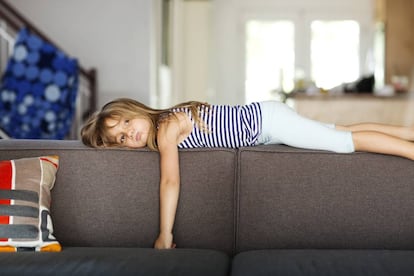 Una niña se tumba aburrida en un sillón. 