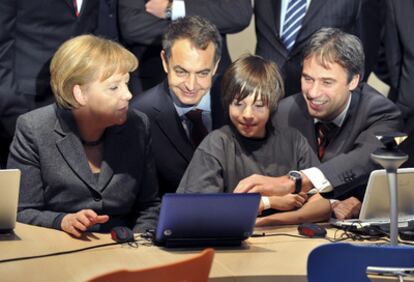 Angela Merkel, José Luis Rodríguez Zapatero, el presidente de Microsoft en Alemania, Achim Berg, y un escolar observan el contenido de un portátil en la feria CeBIT en Hannover.