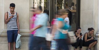 Unos j&oacute;venes consultan el m&oacute;vil en el Paseo de Gracia, en Barcelona