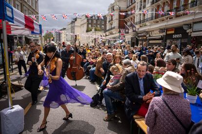 Musicians play their instruments as people sit at long tables to eat their lunch as part of the Big Lunch celebration in London, on May 7, 2023.