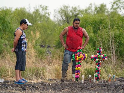 Dos hombres bajo la lluvia contemplan el memorial improvisado cerca del sitio donde fue encontrado el camión de remolque con los migrantes hacinados, el 28 de junio, en San Antonio, Texas, (EEUU).