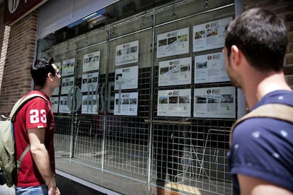 Dos jóvenes observan el escaparate de una empresa inmobiliaria (Madrid).