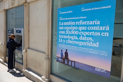 Una mujer saca dinero de un cajero del BBVA en Madrid este martes junto a la publicidad del banco sobre la opa al Banco Sabadell.