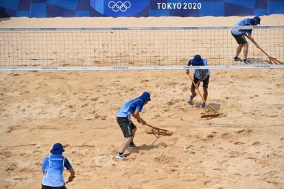 Los asistentes rastrillan la arena entre los sets del partido preliminar masculino de voleibol de playa en el grupo B entre Rusia y México.