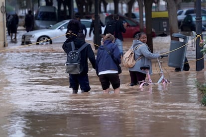 Varias personas caminan con ayudas de cuerdas por una calle inundada en Valencia, este miércoles.  