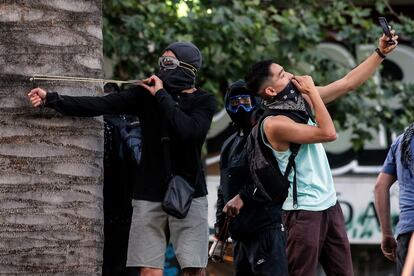 Un manifestante se hace un selfi mientras otro usa una honda contra la policía antidisturbios durante una protesta contra las políticas económicas del Gobierno en Santiago de Chile.