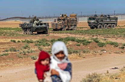 Dos niñas sirias en la ciudad de Darbasiyah (Siria) y vehículos militares durante una patrulla ruso-turca, cerca de la frontera con Turquía, el jueves.