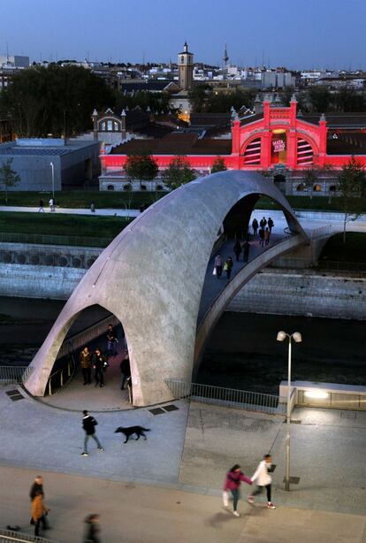 Puente de Madríd Río con el edificio de Matadero iluminado de rojo.