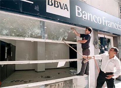 Empleados del banco reparan el establecimiento tras los destrozos provocados durante la <i>cacerolada</i> del jueves.