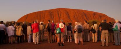 Un grupo de visitantes disfruta del atardecer frente a Ayers Rock (una elevación de 348 metros).