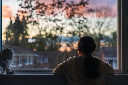 Una niña mira por la ventana de su habitación.