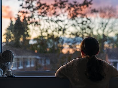 Una niña mira por la ventana de su habitación.