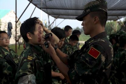 Un instructor cubre la cara de un niño con pintura de camuflaje.