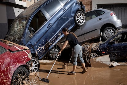 Una mujer arrastra el barro hasta la alcantarilla junto a unos coches destrozados en Aldaia (Valencia), en octubre del año pasado, tras la dana.