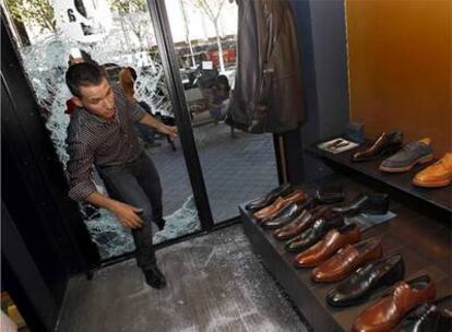 El dueño de la tienda de Serrano 68 entra por el hueco del cristal que los ladrones hicieron en la madrugada del viernes.