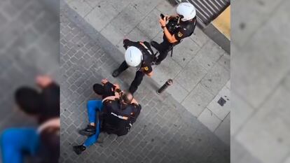 Un agente de Policía Nacional borra vídeos desde el teléfono del detenido, mientras dos agentes le reducen. Imagen extraída de un vídeo distribuido en redes sociales.
