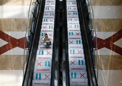 Una mujer, protegida con una mascarilla, sube por las escaleras mecánicas con indicadores de distanciamiento interpersonal, en un centro comercial de Yakarta (Indonesia).