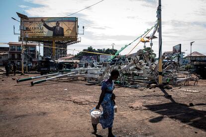 Una mujer camina frente a unas farolas rotas en Conakry durante los incidentes de los últimos días bajo un cartel electoral de Alpha Condé, el pasado 23 de octubre.