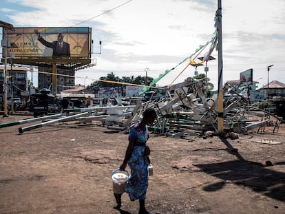 Una mujer camina frente a unas farolas rotas en Conakry durante los incidentes de los últimos días bajo un cartel electoral de Alpha Condé, el pasado 23 de octubre.