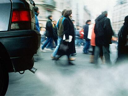 Peatones junto a un vehículo que emite gran cantidad de humo y sustancias contaminantes.