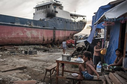 Una familia realiza actividades domésticas en la chabola donde vive desde que perdieron su vivienda por el tifón, en Tacloban. Frente a ellos descansa uno de los barcos varados que aún quedan por la zona.