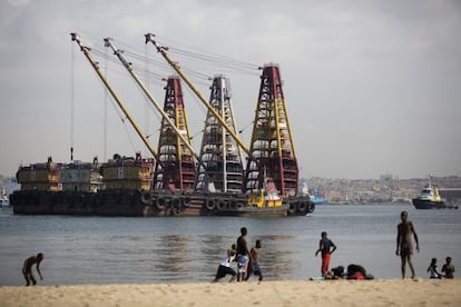 Una barcaza cargada de grúas anclada frente a una playa de Luanda