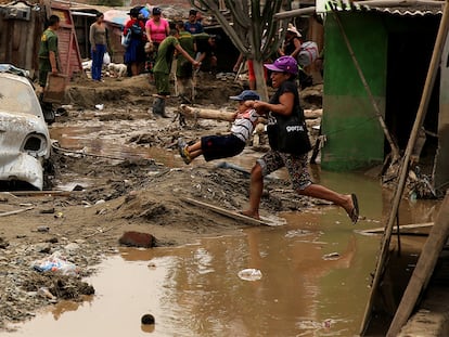 Una mujer ayuda a un niño a cruzar una calle inundada en Huachipa, en Lima (Perú), el 19 de marzo de 2017.