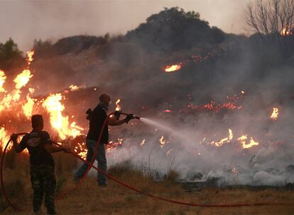 Dos bomberos tratan de apagar un fuego en las cercanías de Atenas. Las llamas avanzan en las últimas horas en un perímetro de 80.000 metros, según un cálculo aproximado de los bomberos