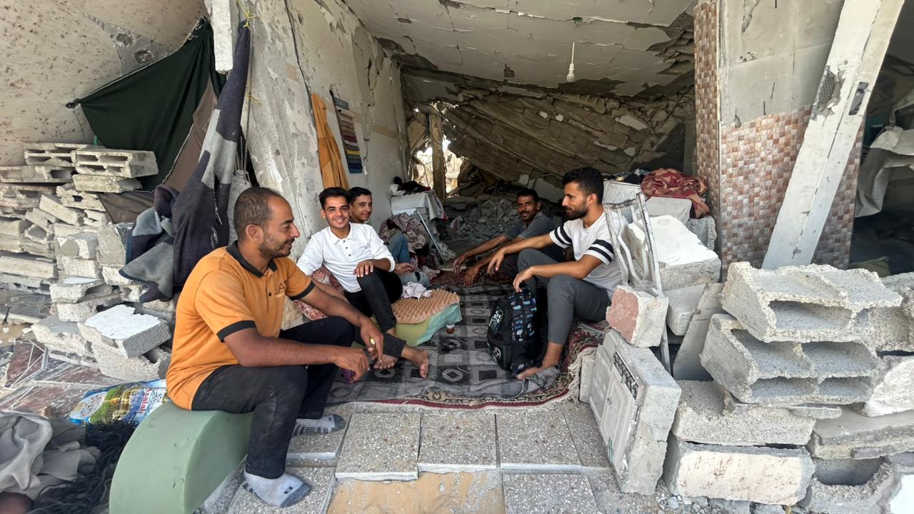 Midhat Wafi, de 38 años, sentado con sus hermanos bajo los restos derrumbados del edificio de cuatro pisos de su familia, cerca de la zona de Katiba, en el centro de Jan Yunis, el 10 de octubre de 2025.