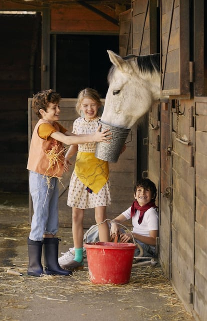 <b>Nicolás</b> va con camiseta de The New Society, chaleco con bolsillos de Melly Mellow, peto de rayas de Bellerose y botas de agua de Pisamonas. A su lado, <b>Stella</b> lleva vestido de flores de Bonpoint, pañuelo atado de The Animals Observatory, calcetines de Caramel Baby & Child, y zuecos de ante de Pisamonas. Sentado en el suelo, <b>Diego </b>viste un mono de The Animals Observatory, camiseta blanca de Tommy Hilfiger, pañuelo de rayas de Louis Louise, calcetines de Bobo Choses y zapatillas de bota de Converse.