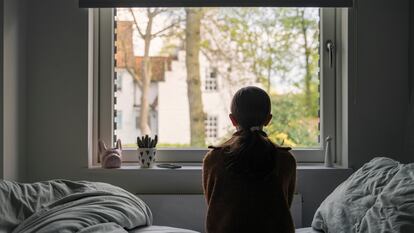 Una niña mira por la ventana de su dormitorio.