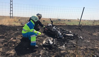 Un bombero y un sanitario observan la motocicleta calcinada.