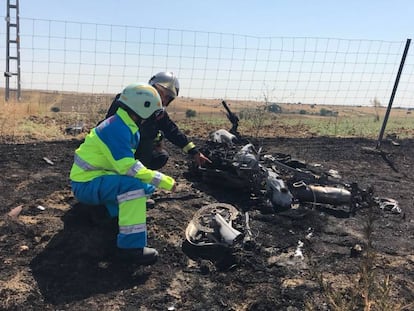 Un bombero y un sanitario observan la motocicleta calcinada.