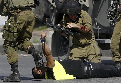 Soldados israelíes de la ONU retienen en el suelo al palestino que ha acuchillado a uno de sus compañeros con el cuchillo que aún sostiene en la mano, en la ciudad palestina de Hebrón.