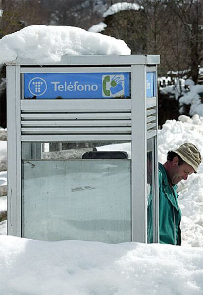 Un hombre se acerca a una cabina casi cubierta por la nieve en el pueblo asturiano de Bezanes.