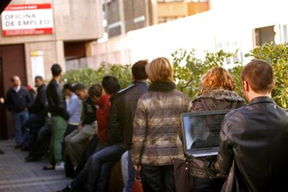 Un joven consulta su ordenador mientras guarda cola ante una oficinia de empleo