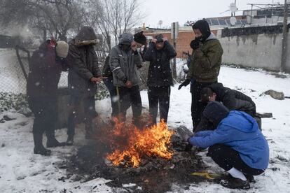 Un grupo de jóvenes se calientan en torno a una hoguera durante la nevada, en la Cañada Real.