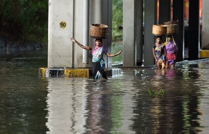 Un grupo de mujeres indias intenta mantener el equilibrio con cestas en sus cabezas mientras atraviesa una calle inundada después de lluvias monzónicas, en Bombay.